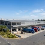 Fotografia aérea de um galpão logístico moderno com diversos caminhões estacionados em docas de carregamento, representando a infraestrutura de ativos do fundo imobiliário BTLG11 em São Paulo.